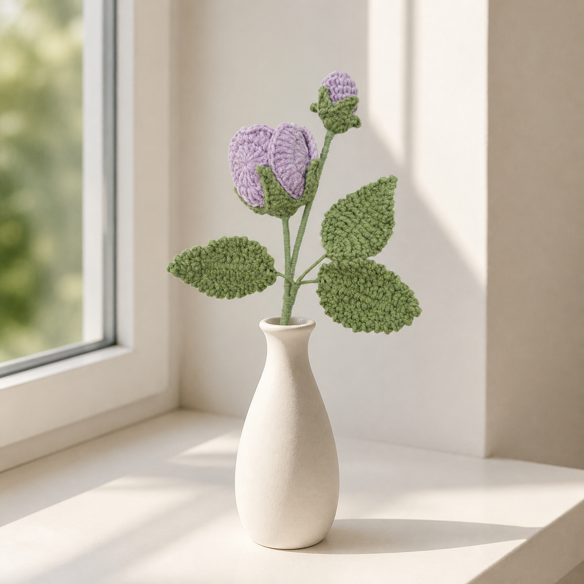 Light purple crochet rose with bud in a white vase by a window