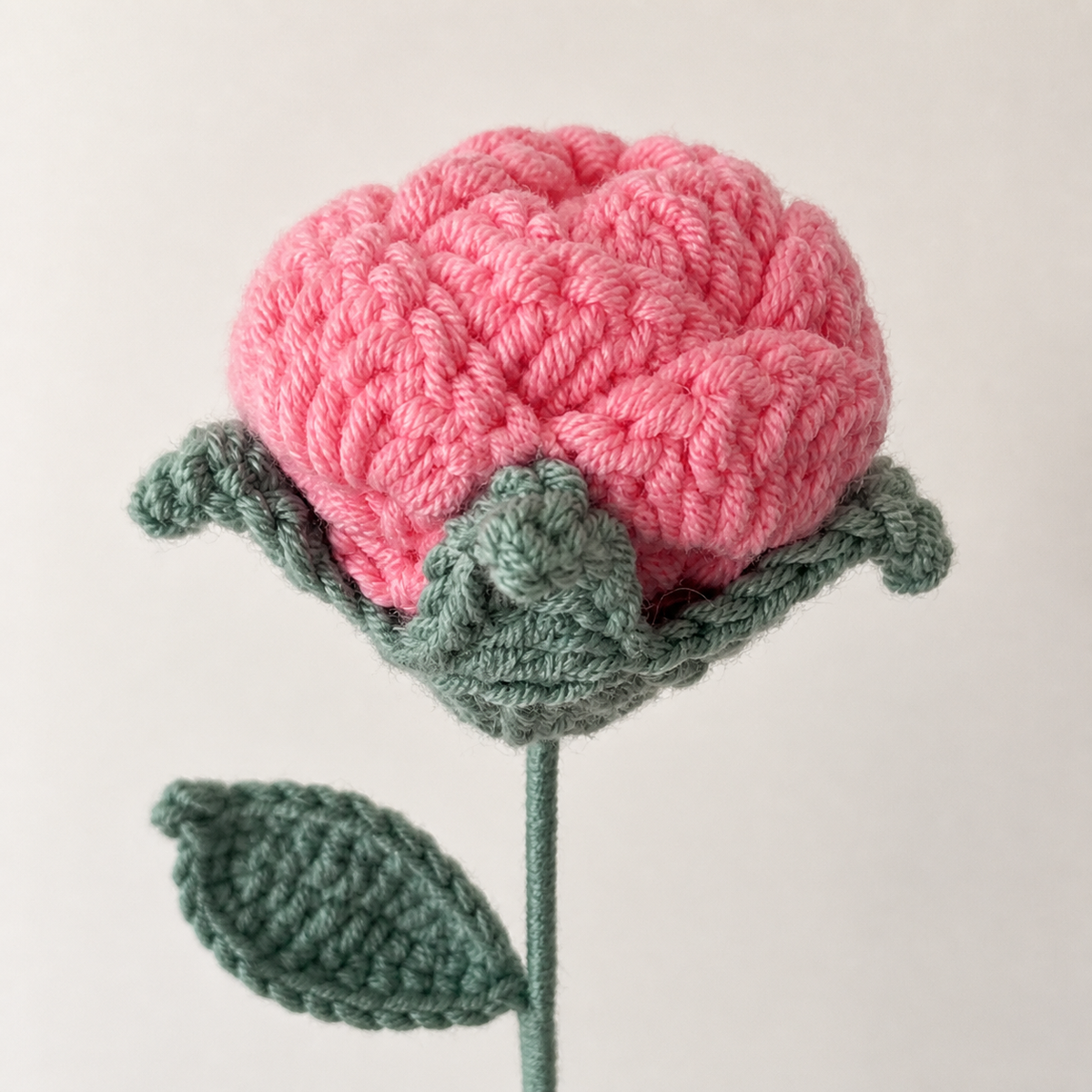 Close-up detail of handmade fashion pink crochet rose petals and teal-gray calyx