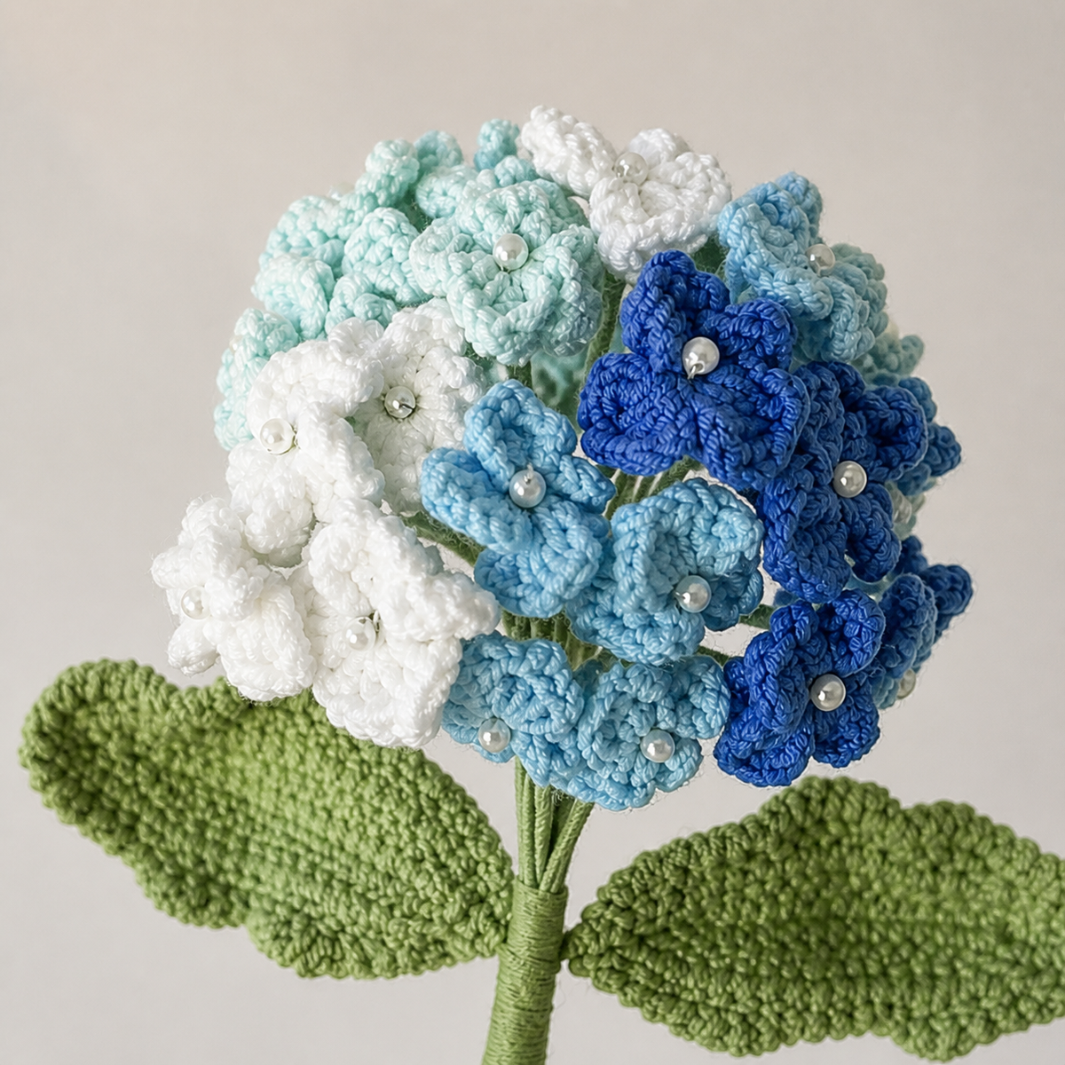 Close-up detail of handmade four-color blue crochet hydrangea blossoms and pearl centers