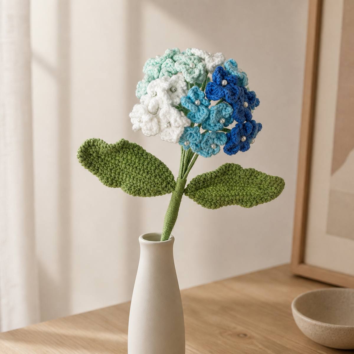 Handmade four-color blue crochet hydrangea displayed in a slim white vase