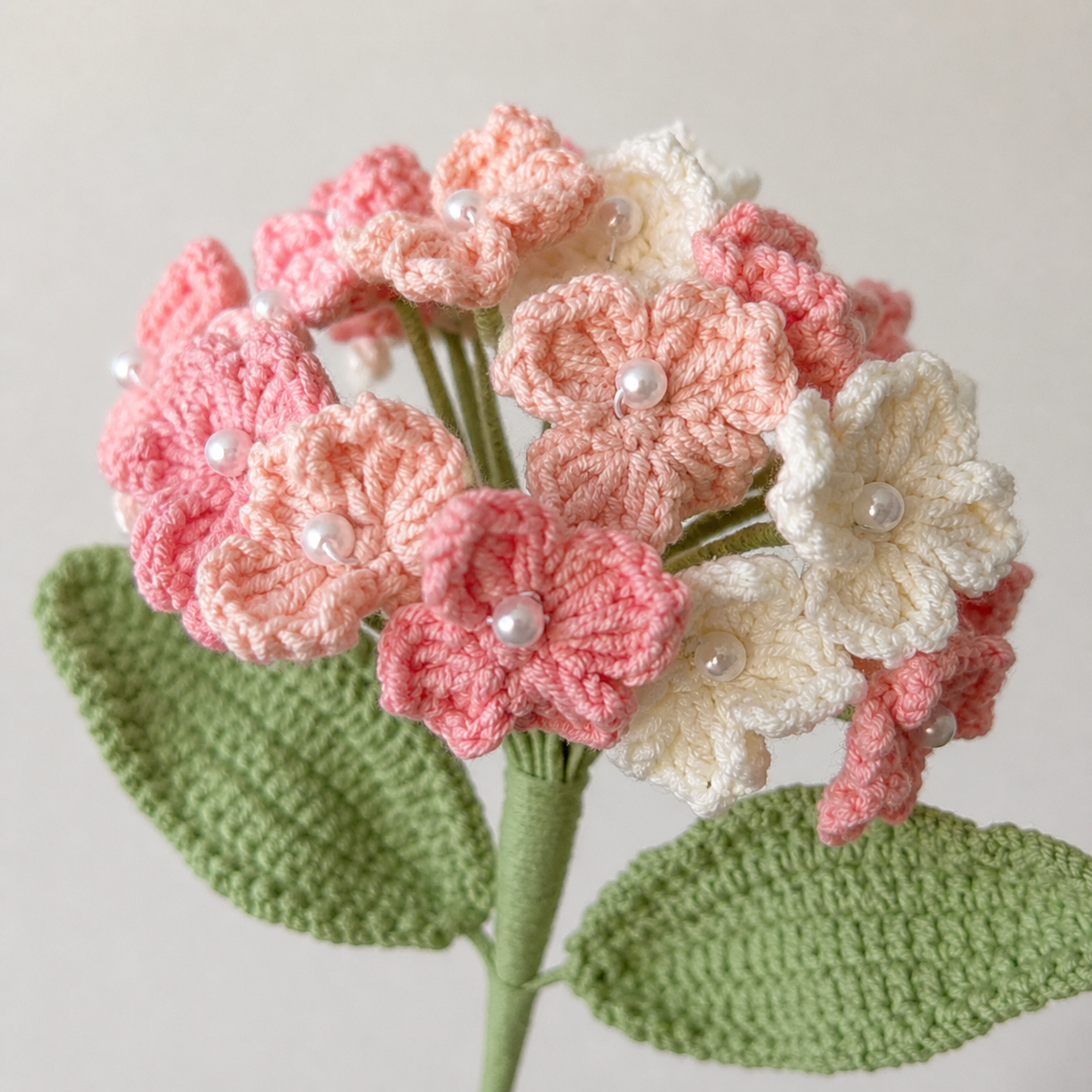 Close-up detail of handmade tricolor pink crochet hydrangea blossoms and pearl centers